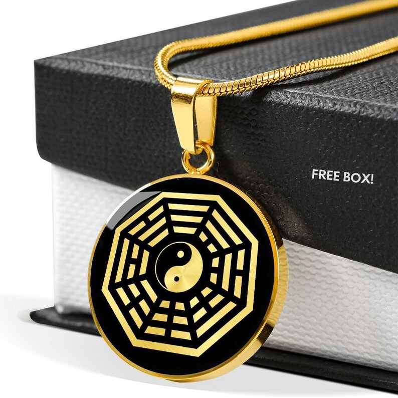 Puede incluir: Collar de oro con un colgante negro y dorado que presenta un s&iacute;mbolo yin yang dentro de un Bagua, un s&iacute;mbolo circular con ocho trigramas, sobre un fondo negro. FREE BOX! est&aacute; escrito en la caja.
