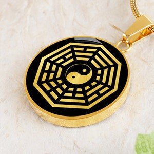 Puede incluir: Collar de oro con un colgante negro y dorado que presenta un s&iacute;mbolo yin yang dentro de un dise&ntilde;o circular de ocho trigramas.