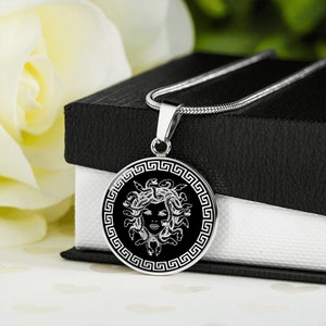 May include: A silver necklace with a round pendant featuring a black and white image of Medusa, the Greek mythological figure with snakes for hair, surrounded by a Greek key border.