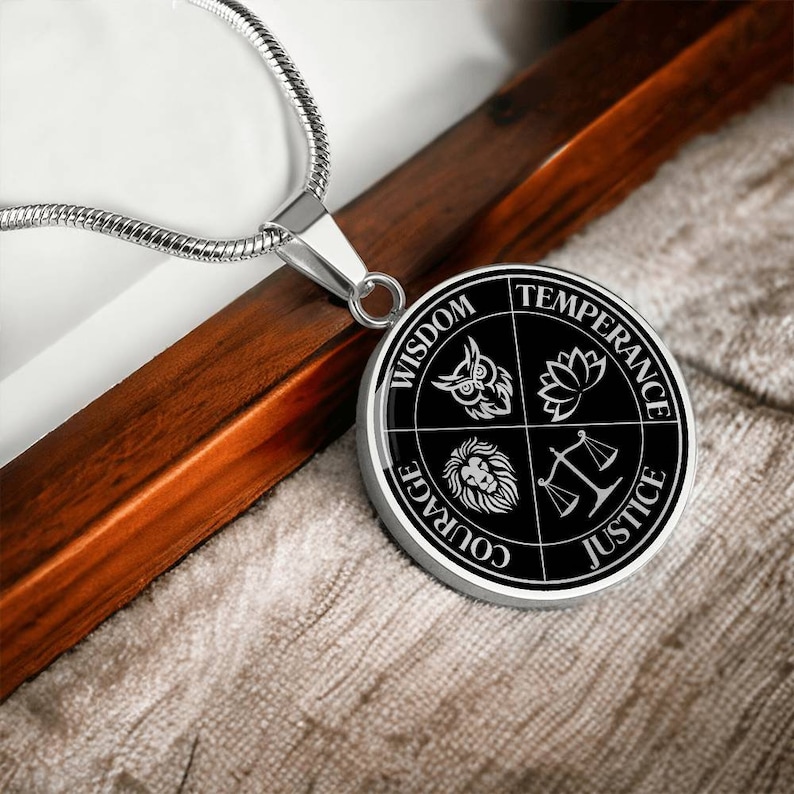 Op de afbeelding: Een zilveren ketting met een ronde zwarte hanger met vier symbolen die wijsheid, matigheid, moed en rechtvaardigheid voorstellen. De symbolen zijn een uil, een lotusbloem, een leeuw en een weegschaal.