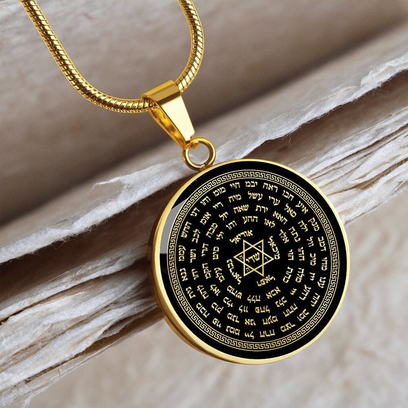 May include: Gold necklace with a round pendant featuring a black background and a gold Star of David with Hebrew text surrounding it.