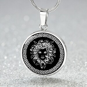 May include: A silver necklace with a round pendant featuring a black and white image of Medusa, the Greek mythological figure with snakes for hair, surrounded by a Greek key border.