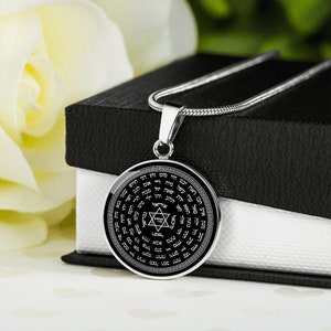 May include: A silver chain necklace with a round pendant featuring a black background with a Star of David and Hebrew text. The pendant is surrounded by a decorative border.
