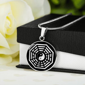 Puede incluir: Un collar de plata con un colgante octogonal de plata que contiene un s&iacute;mbolo yin yang en blanco y negro. El colgante est&aacute; sobre una caja negra con un interior blanco.