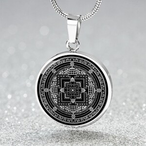 May include: A silver chain necklace with a round pendant featuring a black and white mandala design. The pendant has a silver border and intricate details.