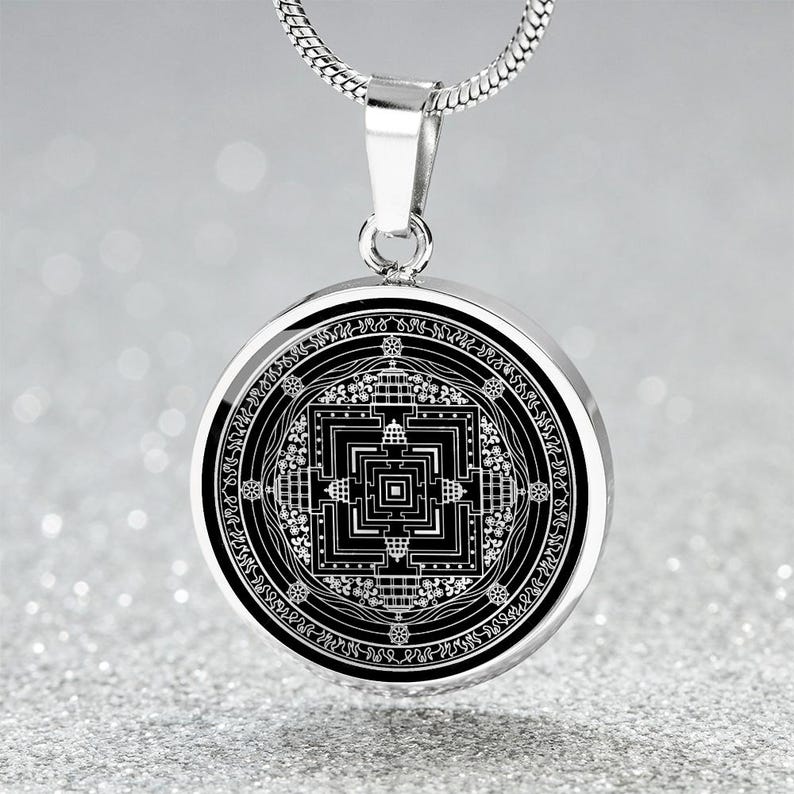 May include: A silver chain necklace with a round pendant featuring a black and white mandala design. The pendant has a silver border and intricate details.