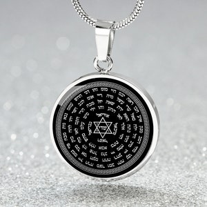 May include: A silver chain necklace with a round pendant featuring a black background and a silver Star of David in the center. The pendant is inscribed with Hebrew text in a circular pattern.