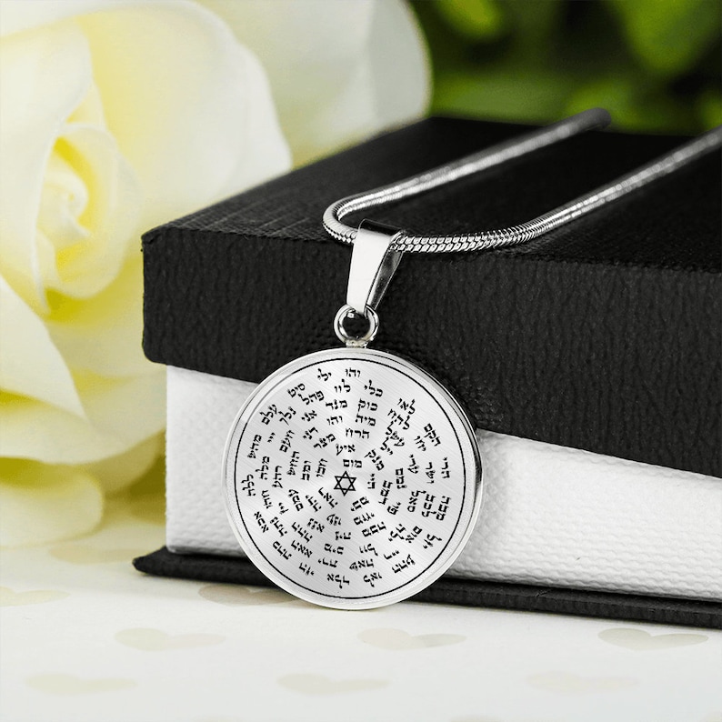May include: A silver necklace with a round pendant featuring a Star of David and Hebrew text. The pendant is inscribed with the words "Malchus, Malchus, Malchus, Adonai, Adonai, Adonai, Elohim, Elohim, Elohim, YHVH, YHVH, YHVH, El, El, El, Shaddai, Shaddai, Shaddai, Tsevaot, Tsevaot, Tsevaot, Echad, Echad, Echad".