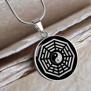 Puede incluir: Un collar de cadena plateada con un colgante redondo que presenta un s&iacute;mbolo yin yang blanco y negro dentro de un s&iacute;mbolo de ocho trigramas blanco sobre un fondo negro.