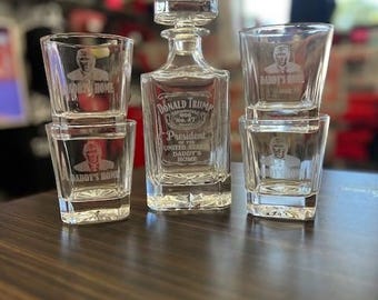 May include: A clear glass decanter with the text "Donald Trump Old No. 47 President of the United States Daddy's Home" etched on the front. Four clear glass shot glasses with the text "Daddy's Home" etched on the front.