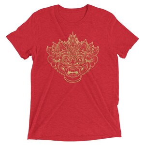 May include: Red t-shirt featuring a gold outline of a Balinese mask with intricate details.