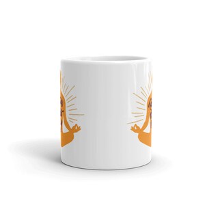 Puede incluir: Taza de caf&eacute; de cer&aacute;mica blanca con una ilustraci&oacute;n amarilla y naranja de una persona en una postura de yoga. El texto "You Got This" est&aacute; escrito en la taza.
