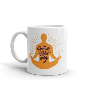 Puede incluir: Taza de cer&aacute;mica blanca con una silueta de una persona en una postura de yoga. La persona es naranja y tiene el texto "Positive Vibes Only" escrito en su espalda en morado.