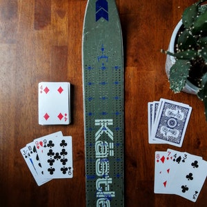 Planche de ski cribbage unique, livrée avec 9 piquets en métal et un jeu de cartes.