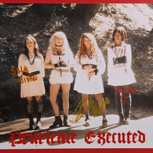 May include: A photograph featuring four individuals in white dresses, standing in front of a blurred natural background. The image has signatures and the text "Prurience Executed" in red gothic font at the bottom. The individuals are wearing black accessories.