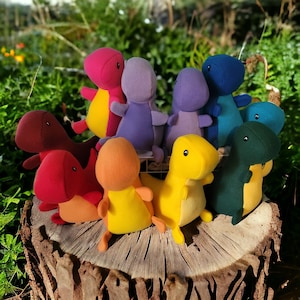 May include: A group of nine plush dinosaur toys in various colors, including purple, red, yellow, blue, and green. The dinosaurs are arranged in a circle on a wooden surface.