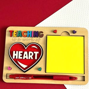 Könnte beinhalten: Holz-Schreibtisch-Organizer mit einem roten Herzen, auf dem "TEACHING is a work of HEART" steht. Er hat einen gelben Haftnotizblock und einen roten Stifthalter.