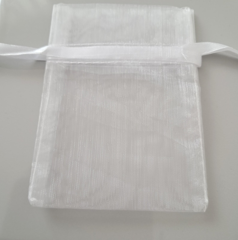 May include: A small, white, sheer organza gift bag with a satin ribbon drawstring closure. The bag is rectangular with a slightly textured appearance. The ribbon is white and is tied in a simple knot.