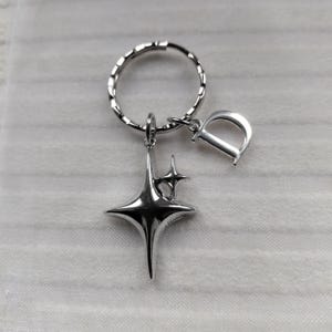May include: Silver-toned keychain featuring a starburst charm and a letter "D" charm. The starburst has a three-dimensional design with multiple points. The keychain ring is a twisted design.