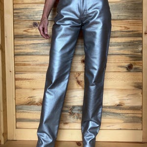 Peut inclure: Pantalon argent&eacute; m&eacute;tallis&eacute; &agrave; coupe droite. Le pantalon a une finition brillante et r&eacute;fl&eacute;chissante et un style classique &agrave; cinq poches. Le pantalon est pr&eacute;sent&eacute; sur un fond en bois.
