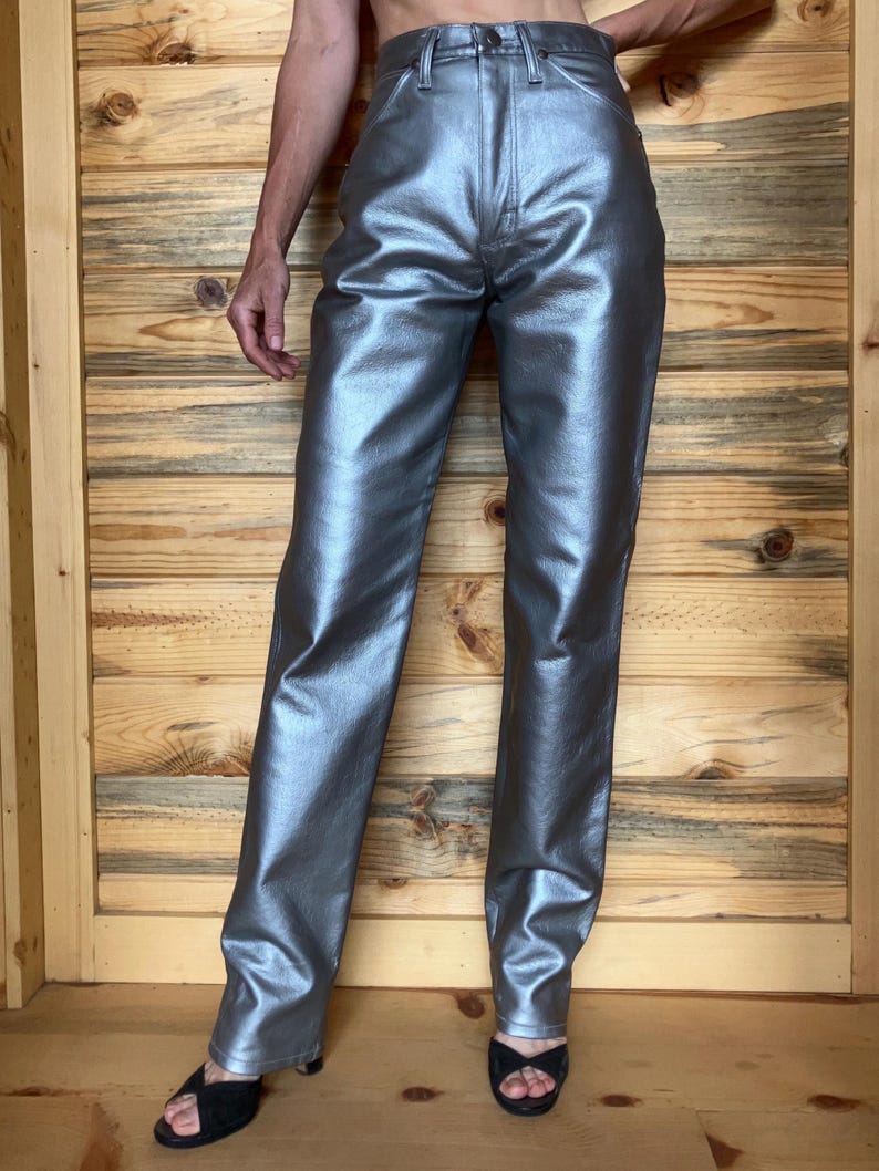 Peut inclure: Pantalon argent&eacute; m&eacute;tallis&eacute; &agrave; coupe droite. Le pantalon a une finition brillante et r&eacute;fl&eacute;chissante et un style classique &agrave; cinq poches. Le pantalon est pr&eacute;sent&eacute; sur un fond en bois.