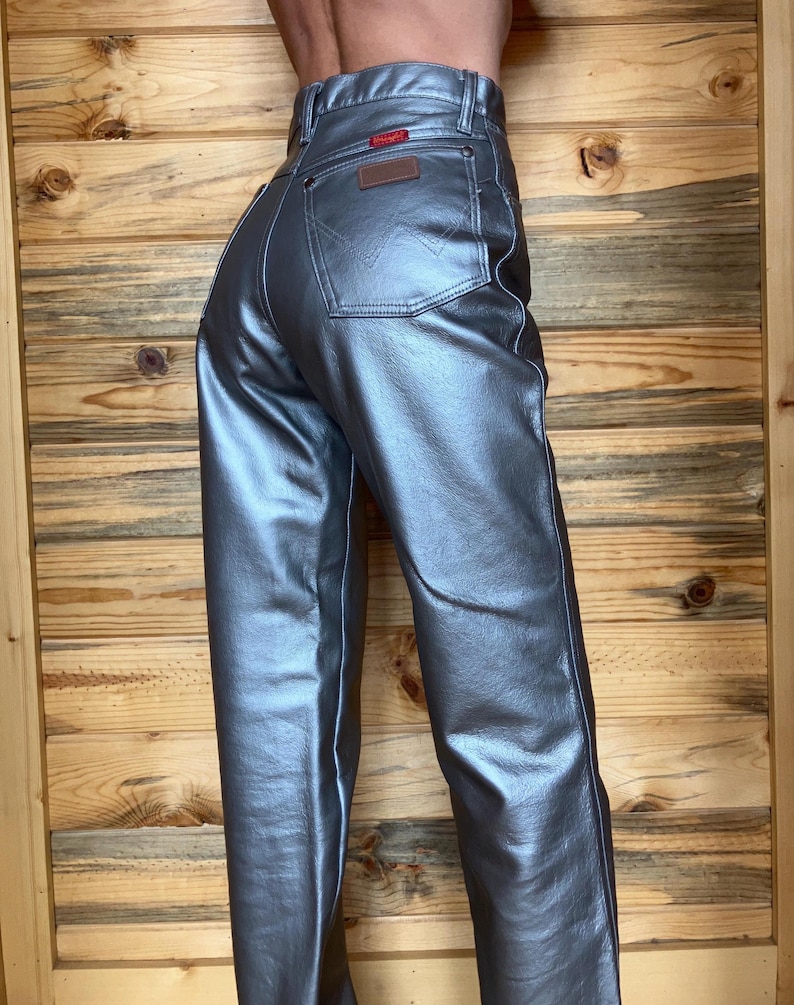 Peut inclure: Un jean Wrangler m&eacute;tallis&eacute; argent&eacute; &agrave; taille haute avec une conception classique &agrave; cinq poches. Le jean pr&eacute;sente un patch en cuir marron et une &eacute;tiquette Wrangler rouge sur la poche arri&egrave;re. Le pantalon est en similicuir brillant.