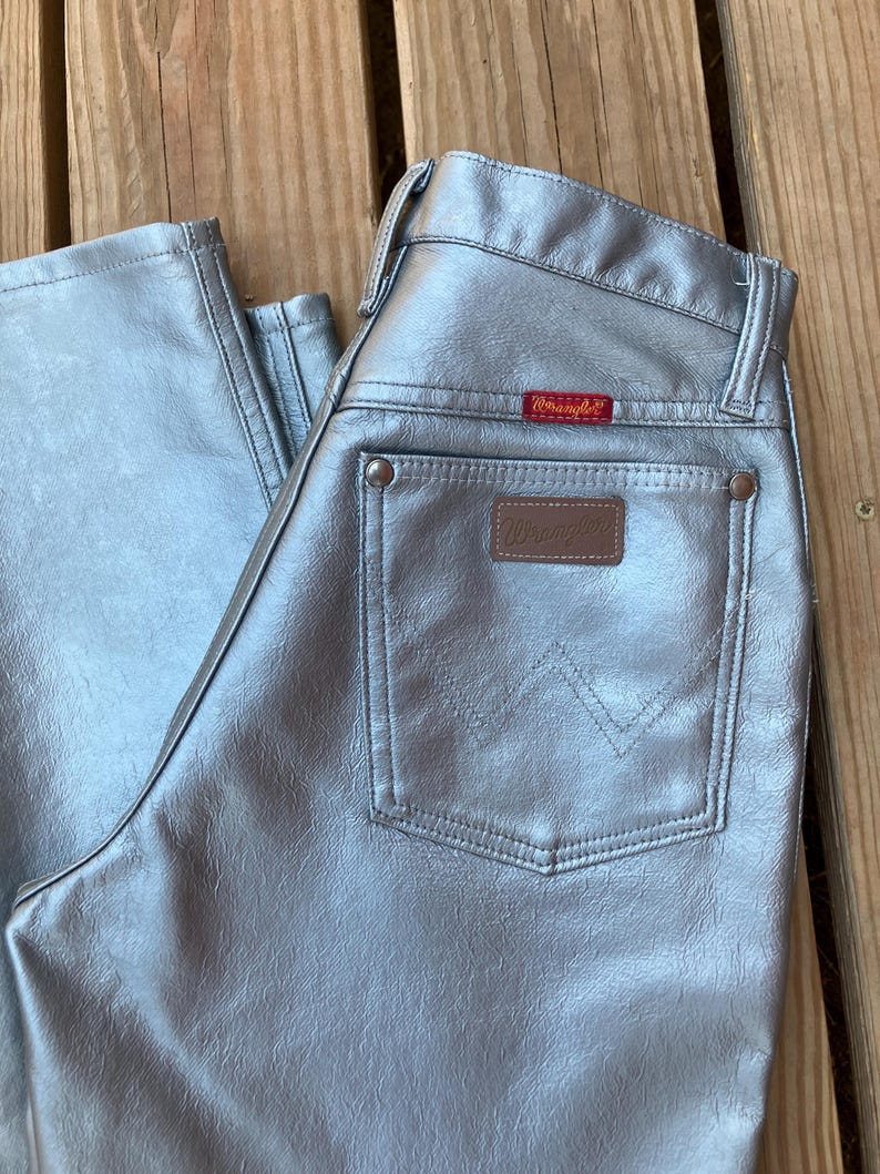 Peut inclure: Un pantalon Wrangler argent&eacute; avec une conception classique &agrave; cinq poches. Le jean pr&eacute;sente un patch en cuir marron et une &eacute;tiquette Wrangler rouge. La finition m&eacute;tallique donne au pantalon un aspect unique et accrocheur.