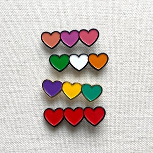 May include: Set of six heart-shaped enamel pins in various colors, including red, pink, purple, green, yellow, and orange. The pins are arranged in three rows of two, with each row featuring a different color combination.