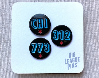 May include: Three black enamel pins with blue and red lettering. The pins feature the words "CHI", "312", and "773". The pins are on a white background with the text "BIG LEAGUE PINS".