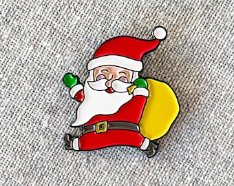 May include: A red and white enamel pin of Santa Claus with a white beard and a yellow sack. He is wearing a red suit with a black belt and a green hat.