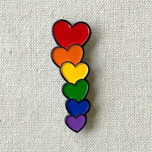 String of Hearts Pride enamel pin – This cheery pin leaves a trail of hearts wherever you wear it! Pride gift. Cute rainbow heart gift.