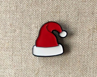 Può includere: Spilla in smalto rosso e bianco a forma di cappello di Babbo Natale.