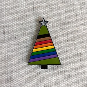 Könnte beinhalten: Eine grüne Weihnachtsbaum-Anstecknadel mit einem Regenbogenstreifenmuster und einem silbernen Stern oben.