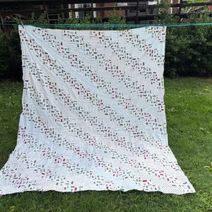 Può includere: Una trapunta rettangolare con sfondo bianco e un motivo ripetitivo di piccoli punti neri. La trapunta è decorata con strisce diagonali composte da piccoli pezzi di tessuto rettangolari nei toni del rosso, del blu e del grigio.