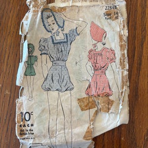 May include: A vintage sewing pattern envelope labeled 2284B, Size 14, Bust 32. The illustration shows a romper with puff sleeves and a square neckline, accompanied by a matching bonnet. The paper is worn and torn, displaying the price of 10 cents.