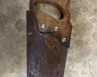 May include: A vintage hand saw with a wooden handle and a rusty, toothed blade. The handle is attached with three silver screws. The saw blade shows signs of age and wear, with a dark, weathered appearance. A tool for woodworking.
