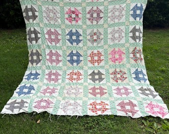 Può includere: Una grande trapunta patchwork caratterizzata da un motivo a blocchi ripetuti in vari colori, tra cui rosso, blu, grigio e rosa. I blocchi sono separati da un tessuto verde chiaro con una piccola stampa floreale bianca, creando una griglia.