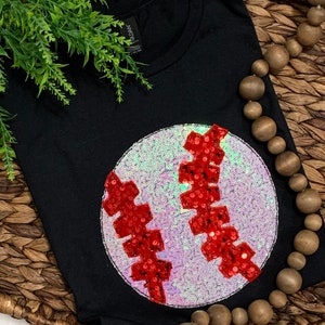 May include: Black t-shirt with a large white and red sequined baseball graphic.
