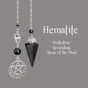 Può includere: Due pendoli di ematite appesi su sfondo grigio. Uno presenta un ciondolo a pentacolo argentato e un ciondolo a forma di volto. L'altro è un cristallo sfaccettato grigio scuro. Il testo recita "Ematite" e descrive le proprietà della pietra.