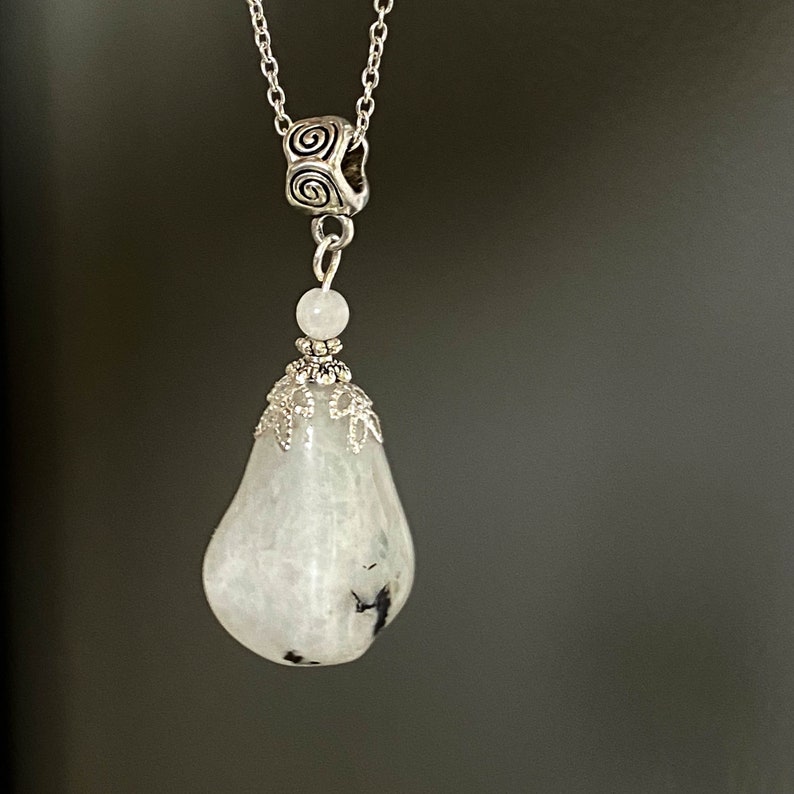 May include: A silver necklace featuring a pear-shaped, white and gray gemstone pendant. The pendant is suspended from a delicate chain and adorned with decorative silver accents. The gemstone has dark gray inclusions.