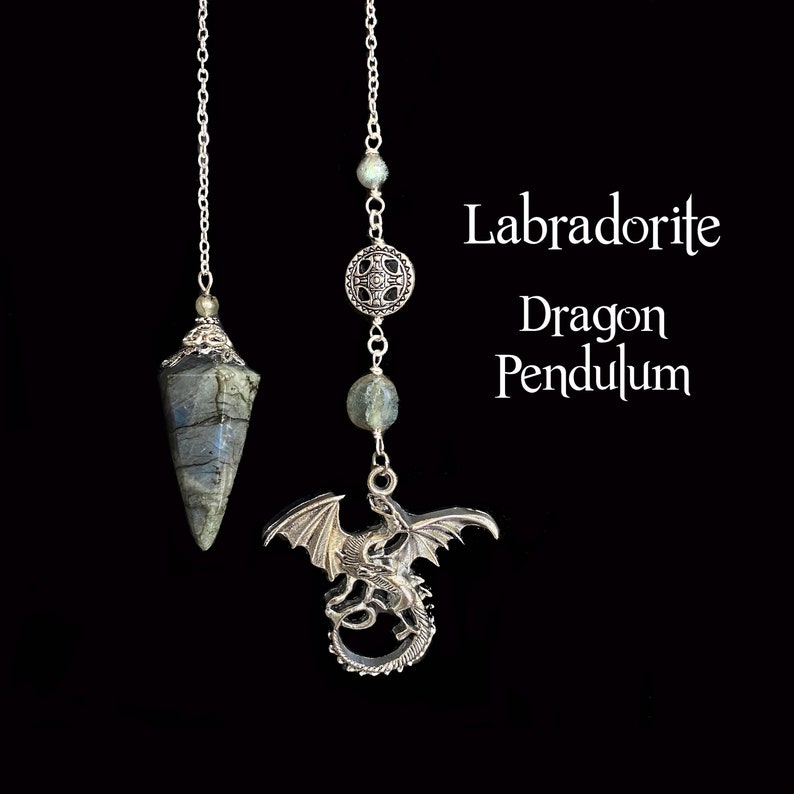 K&ouml;nnte beinhalten: Zwei Labradorit-Drachenpendel h&auml;ngen vor einem schwarzen Hintergrund. Eines hat einen facettierten Stein, das andere einen silbernen Drachenanh&auml;nger. Der Text "Labradorite Dragon Pendulum" ist in Wei&szlig; dargestellt.
