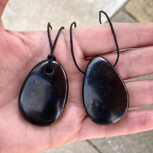 May include: Two polished, black teardrop-shaped pendants with a glossy finish. Each pendant has a small hole at the top and is strung on a black cord. The pendants are displayed against a neutral background.