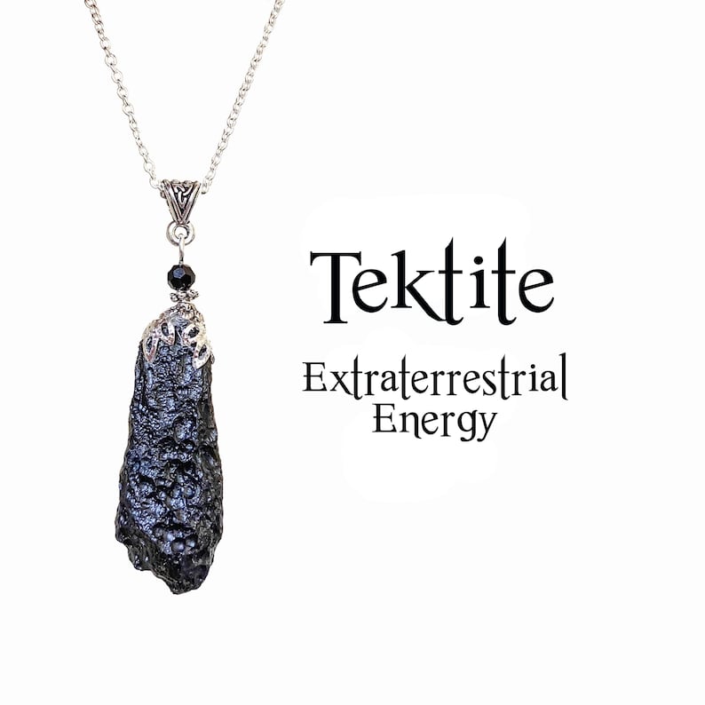 May include: A black tektite pendant necklace with a silver chain. The tektite is a dark, textured stone with a silver cap and a small black bead. The text "Tektite Extraterrestrial Energy" is displayed in black.