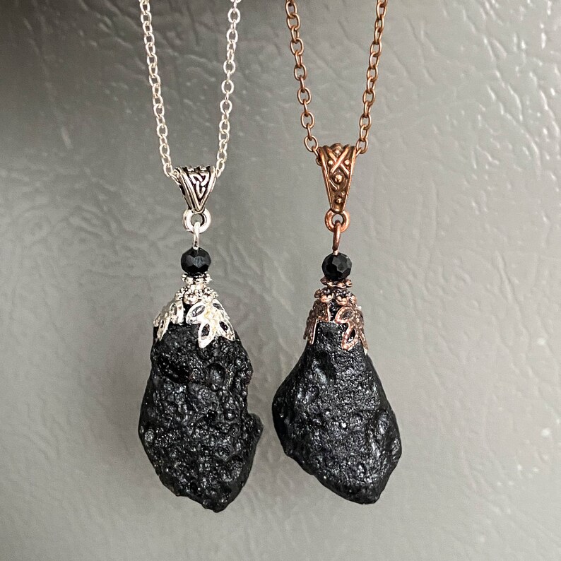 May include: Two black stone pendant necklaces. One has a silver chain and accents, the other a copper chain and accents. Each pendant is a rough, irregular shape, with a small black bead above the stone.