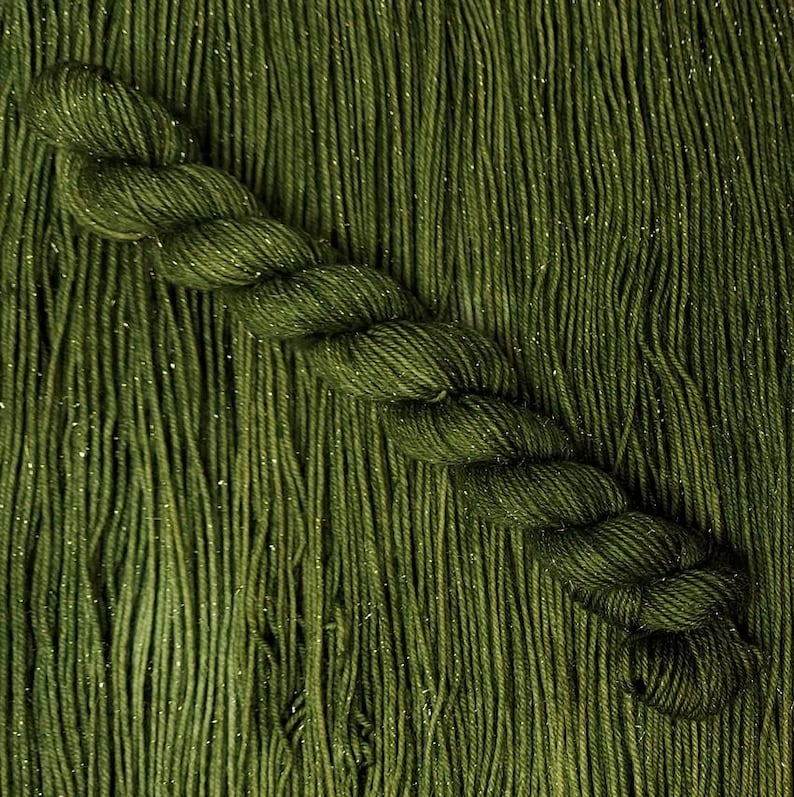 May include: A close-up of a deep green yarn with a subtle sparkle. The yarn is twisted into a braid and has a soft, fuzzy texture.