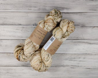May include: Two skeins of cream-colored yarn with brown and green flecks. The yarn is labeled "Soft & Sweet" and "Cozy Wool" with a QR code.