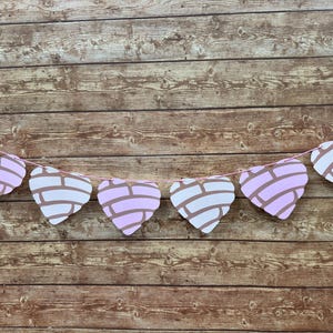 May include: A garland of heart-shaped decorations in pink and white, with brown accents, strung on a pink string. The hearts are set against a wooden background.