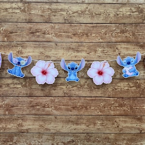 Op de afbeelding: Een slinger met het personage Stitch, surfplanken en hibiscusbloemen. De blauwe Stitch-figuren staan in verschillende poses, sommigen houden ijs of een ukelele vast. De surfplanken zijn paars met witte bloempatronen.