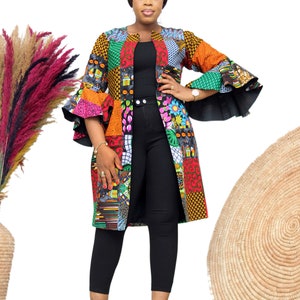 Può includere: Una lunga giacca patchwork colorata con una maglia nera e pantaloni neri. La giacca ha un collo a V e maniche lunghe con maniche a campana. La persona indossa tacchi neri.
