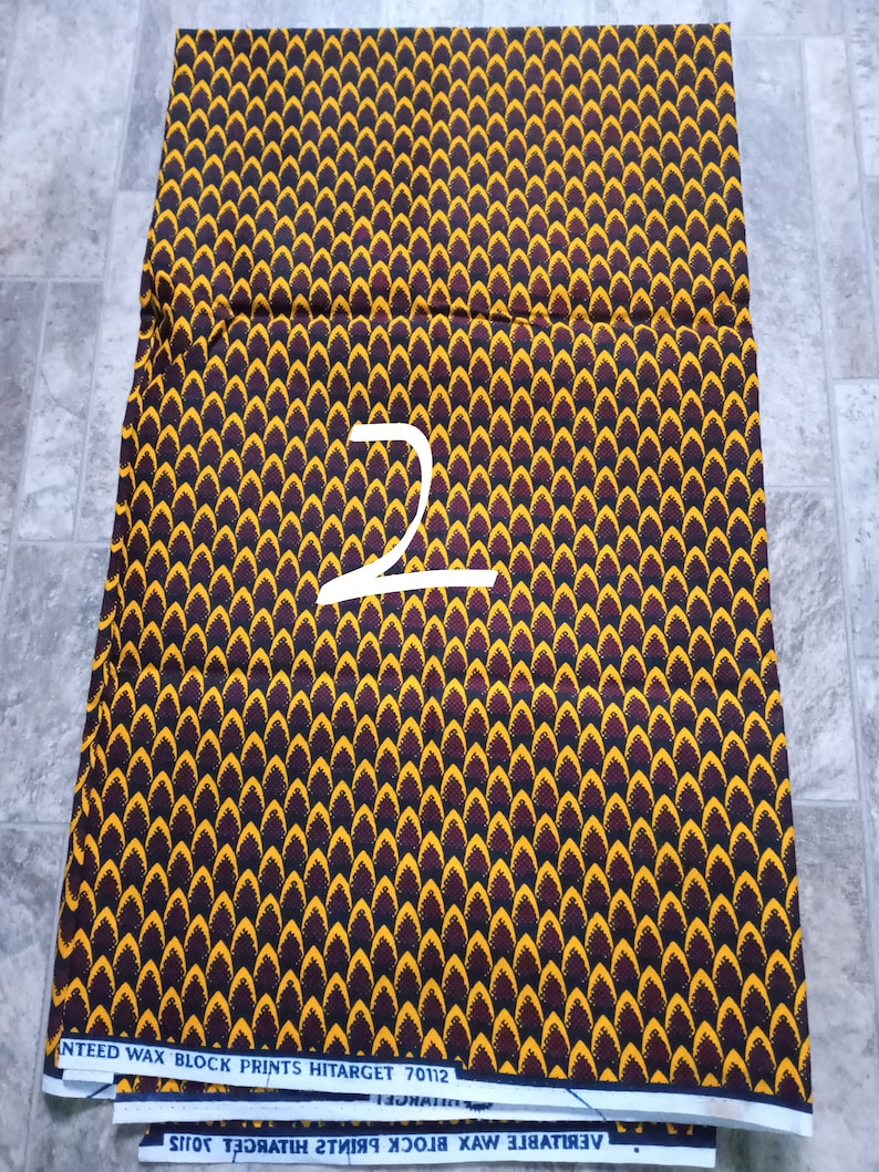 May include: A stack of fabric with a black, yellow, and red pattern. The fabric is labeled "VERITABLE WAX BLOCK PRINTS HITarget 70112" and "ANTEED WAX BLOCK PRINTS HITarget 70112".